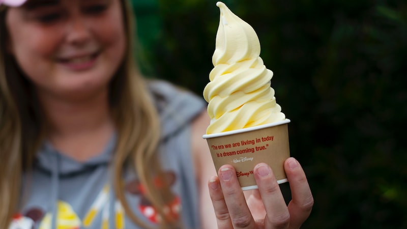 A girl holding a tall swirl of soft serve Dole whip in a Disney Parks cup
