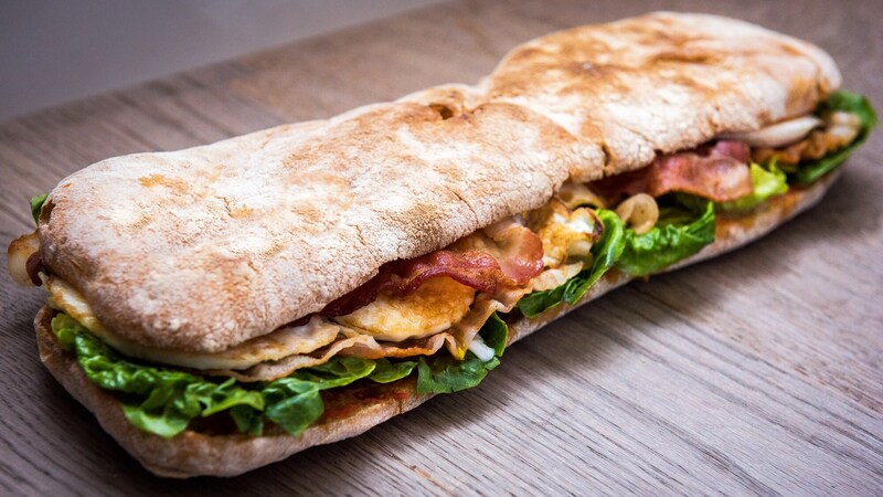 A long sandwich with thin bread, bacon, lettuce and other ingredients
