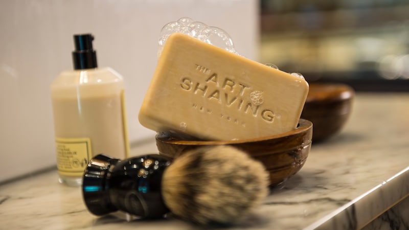 Grooming products at The Art of Shaving shop featuring a shaving brush, soap, wooden bowl and balm