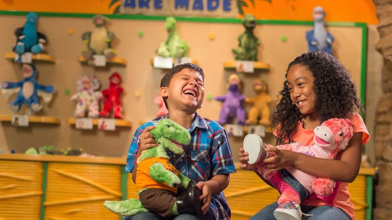 A boy and a girl laugh as they each hold a plush dinosaur toy