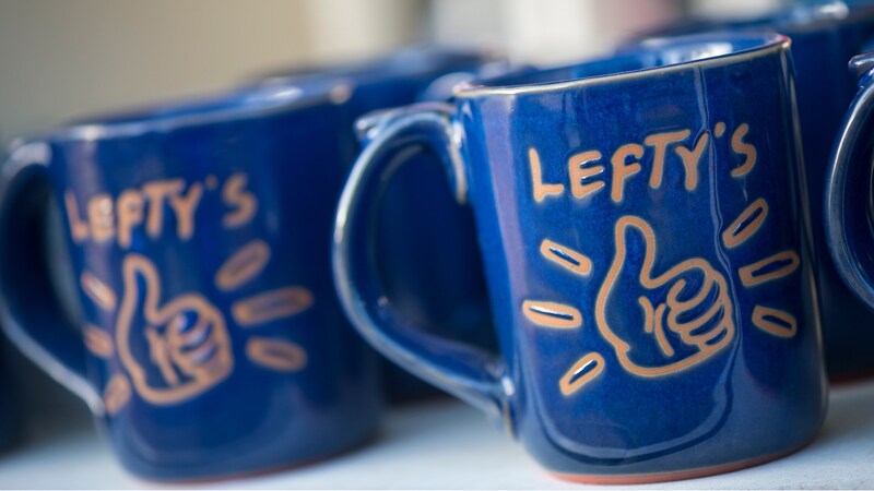 Logo terra-cotta left-handed mugs on a shelf within Lefty’s The Left Handed Store at Disney Springs
