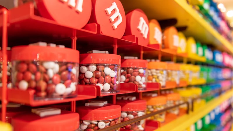 Clear canisters of em and ems are arranged on the shelves of a wall display to create a rainbow effect