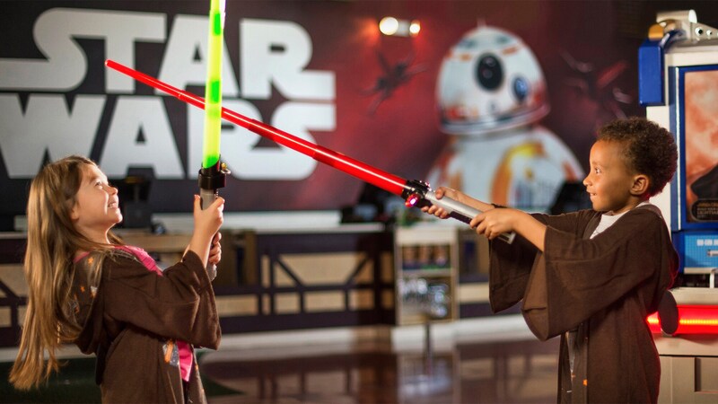 A young girl and boy play dressed as younglings play with light sabers