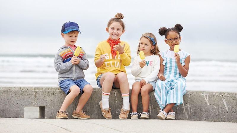 Four young children eating ice pops sit on a concrete curb by the ocean