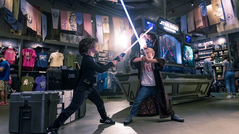 Surrounded by Star Wars merchandise displays, 2 young boys pretend to battle with lightsabers 