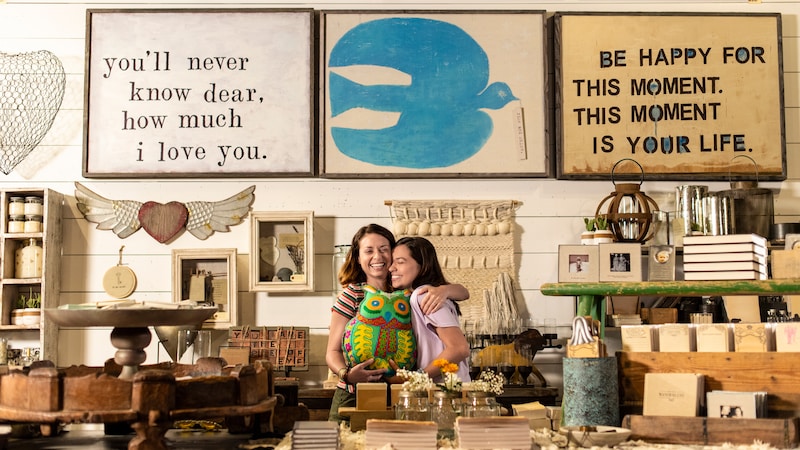 A mom hugs her teen daughter while holding a large owl pillow amidst other home decor items at Sugarboo