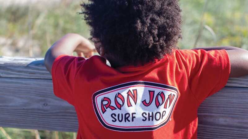 A child wears a shirt with words that read Ron Jon Surf Shop