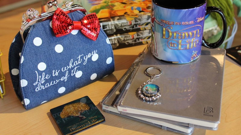 Merchandise for Cirque du Soleil Drawn to Life including a coffee mug, notebook and keychain