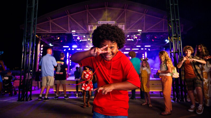 A young child dancing in front of an outdoor concert stage at night
