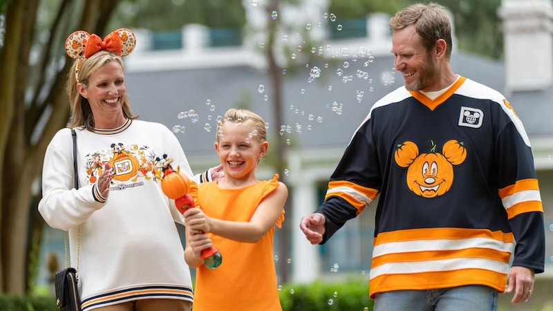 A family of 3 walking outdoors in Mickey's Not So Scary Halloween Party merchandise