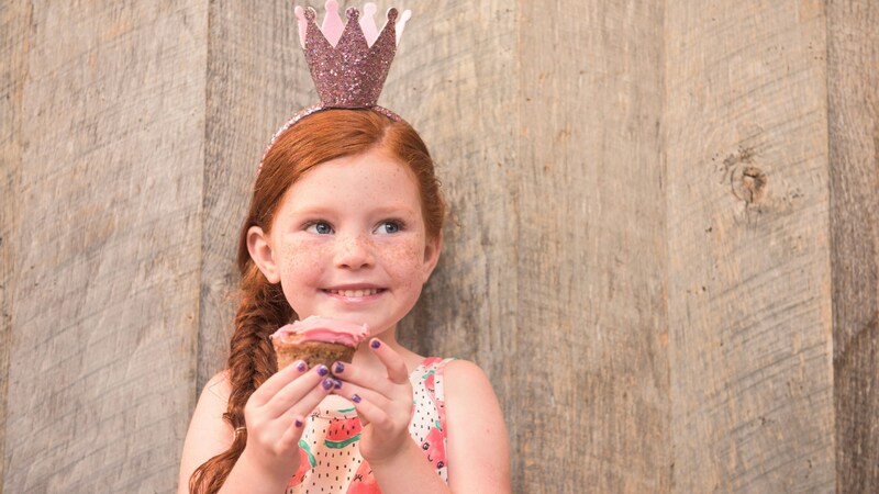 A young girl smiling as she holds a cupcake near her face