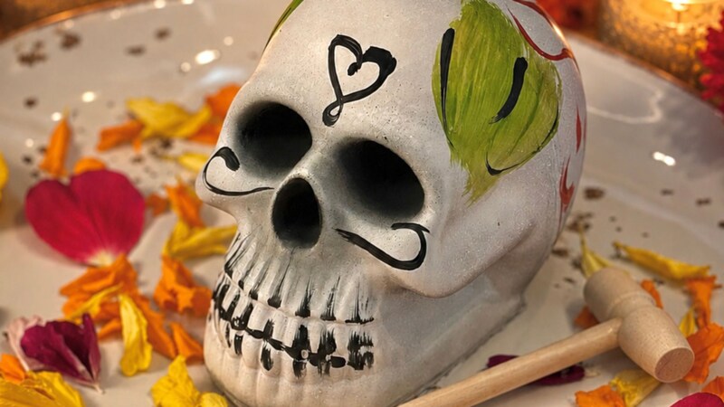A chocolate Dia de los Muertos skull plated next to a wooden mallet, surrounded by candles and decor