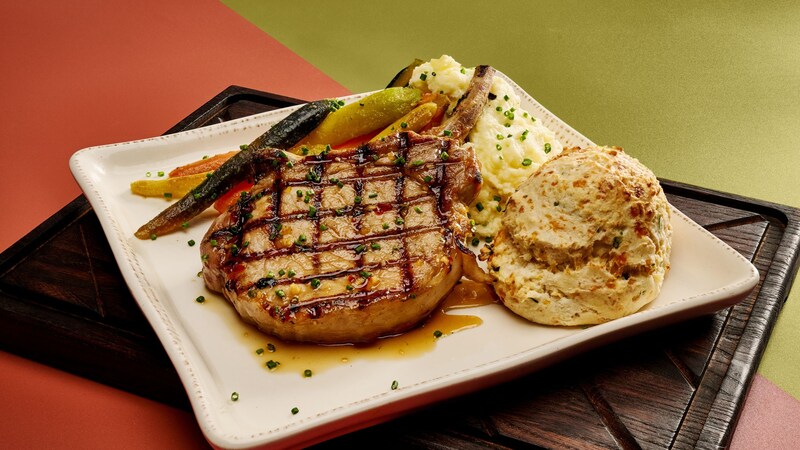 A pork chop plated with mashed potatoes, vegetables and a biscuit