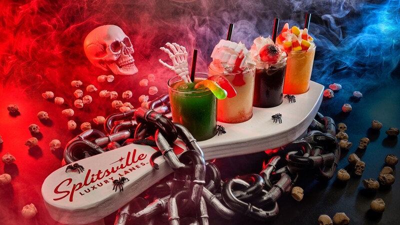 A Halloween themed drink flight served on a bowling pin shaped tray with chains and skeleton skull decor