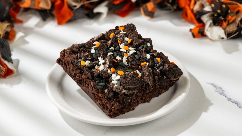 A Halloween brownie topped with cookie pieces, passion fruit crispy pearls and a chocolate coin