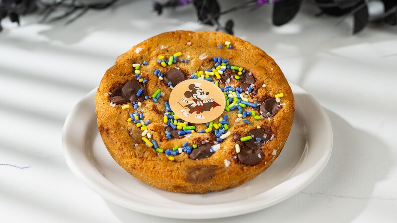 A chocolate chip cookie with sprinkles and a Halloween themed Mickey Mouse chocolate coin