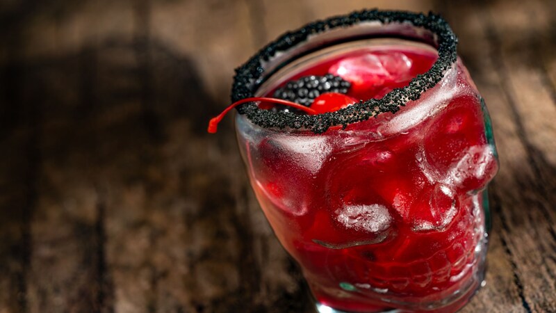 A cocktail served in a skull glass, topped with a cherry 