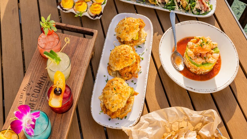 A table at Chef Art Smith’s Homecomin’ in Disney Springs filled with cocktails and plates with deviled eggs, shrimp cocktail, chicken biscuits and fried green tomatoes with shaved ham and greens