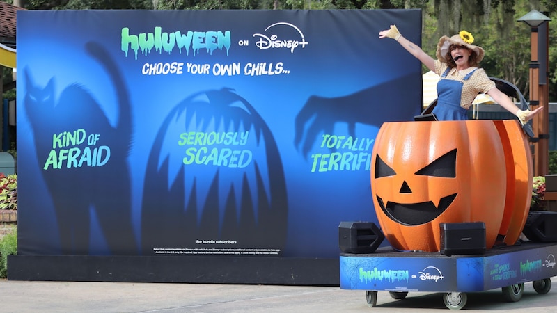 A roaming DJ pumpkin next to a large billboard for Huluween on Disney Plus with the words, ‘Choose your own chills’