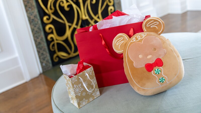 Un Squishmallow de Mickey Mouse de jengibre junto a dos bolsas de regalo