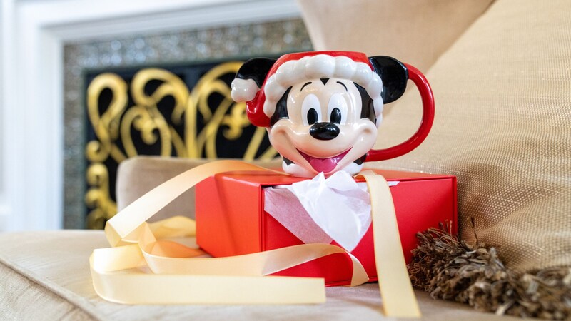 Una taza de Mickey Mouse vestido de Santa sobre una caja de regalo