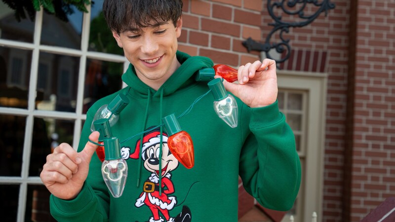 Un Visitante con una sudadera con capucha de Mickey Mouse vestido de Santa y un collar gigante con luces	