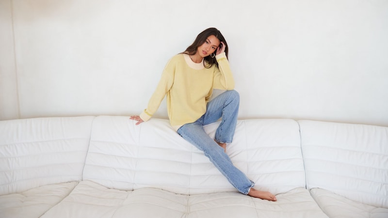 A young woman in jeans and an oversized sweater sitting on top of a couch