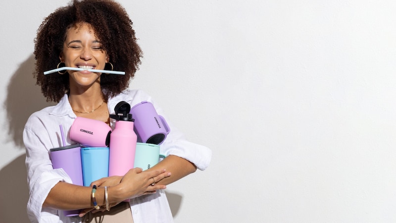 A smiling young woman holding an assortment of Corkcicle drinkware	