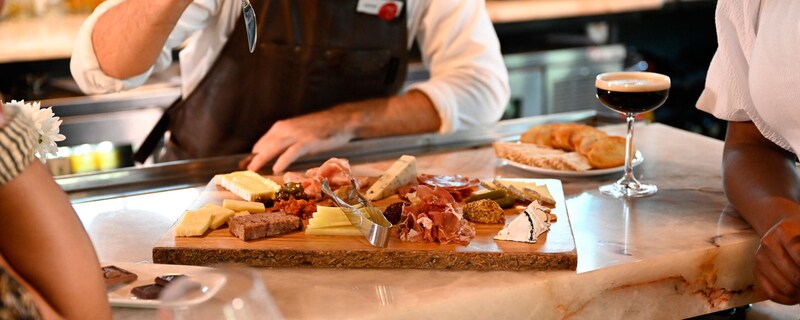 A chef offers 2 people samples from a charcuterie plate