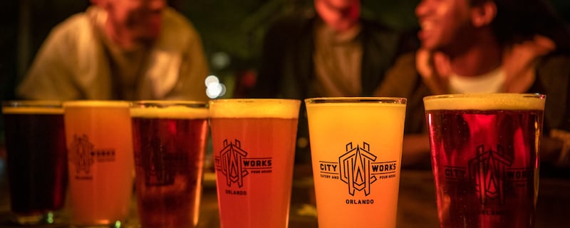 Three friends sitting at a table with glasses filled with various beers from City Works Eatery and Pour House Orlando