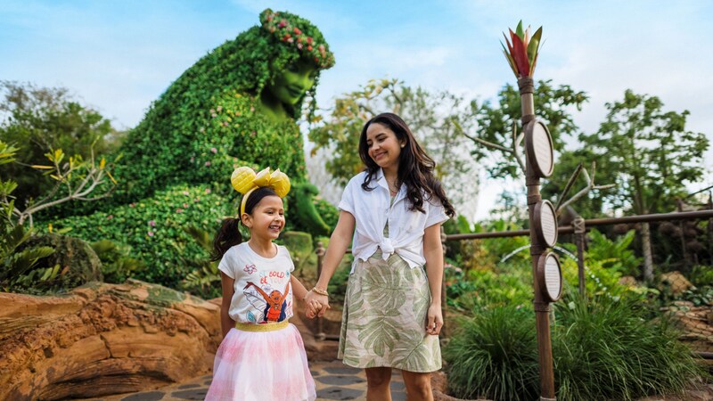 Two Guests walk hand in hand past the tall Te Fiti topiary at the Journey of Water, Inspired by Moana attraction