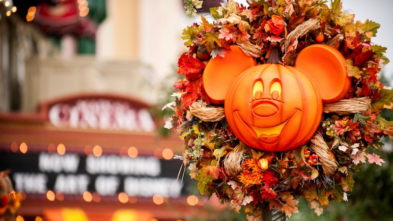 Una corona iluminada con una calabaza de Halloween de Mickey Mouse decorada con hojas y flores de otoño en Magic Kingdom Park