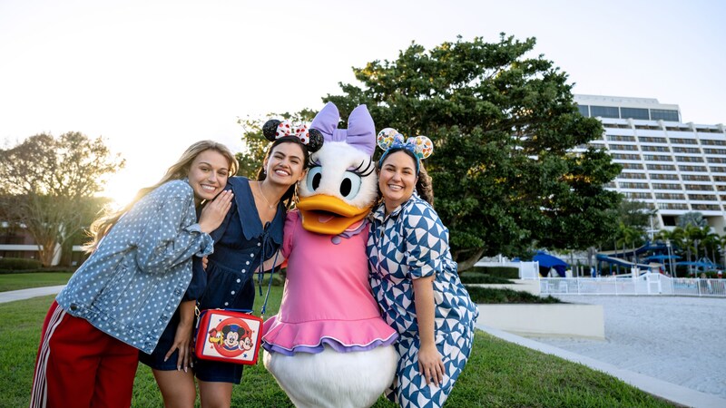 Three Guests posing with Daisy Duck in front of Disney’s Contemporary Resort