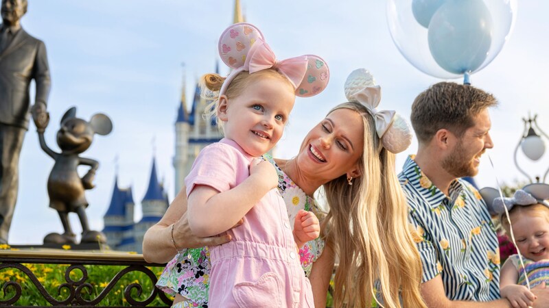 A mother and daughter wearing Minnie Mouse ear headbands pose near the Partners statue and Cinderella Castle
