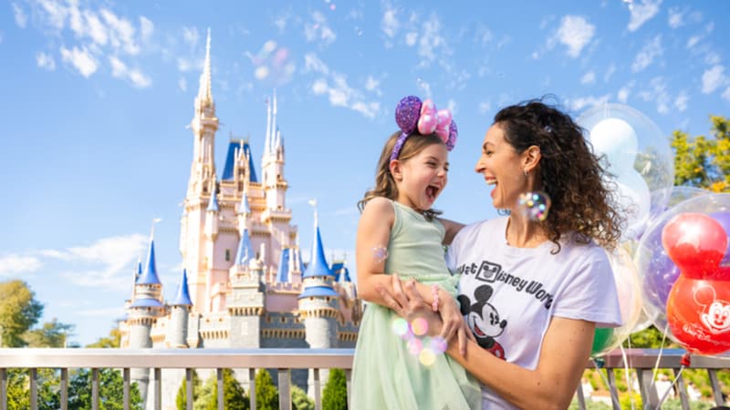 A mother holding her smiling daughter in her arms in front of Cinderella Castle