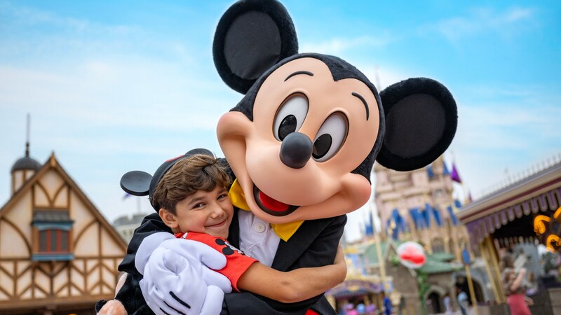 A boy wearing a Mickey Mouse ear hat gets a hug from Mickey Mouse himself