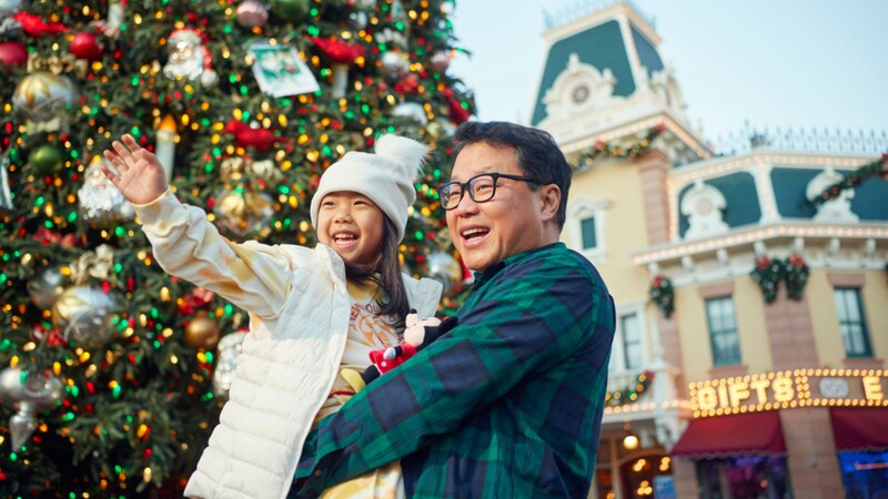 A smiling dad and daughter in front of a Christmas tree  