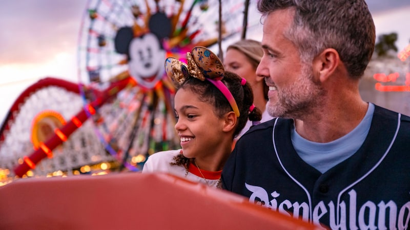 A father and daughter smiling together with Pixar Pal A Round in the distance