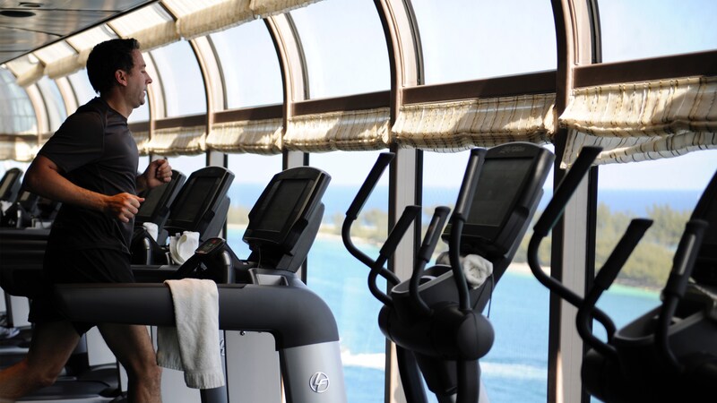 A man running on a treadmill situated in front of a window that looks out to the ocean