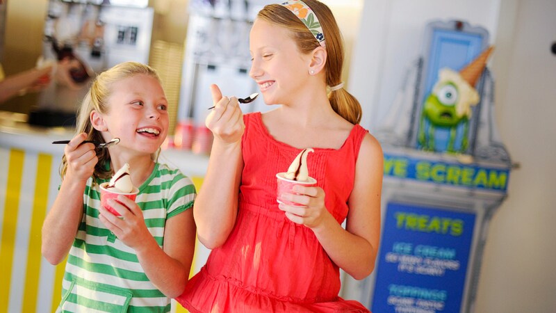 2 young girls smile at each other while eating soft serve ice cream