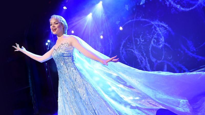 Elsa from Frozen performing on stage in a long gown and flowing cape