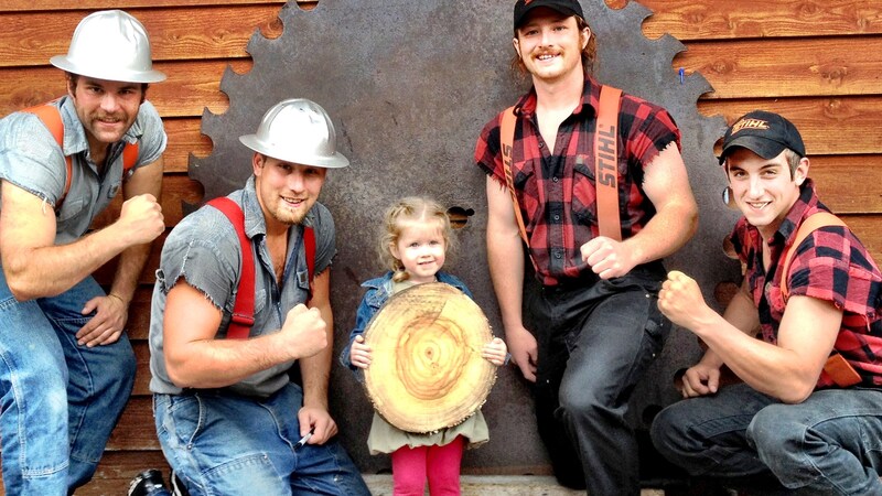 Uma criancinha posa com uma equipe de lenhadores