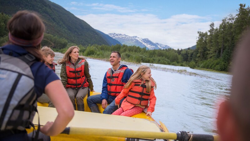 A family in lifejackets rafting on a lake surrounded by mountains and trees
