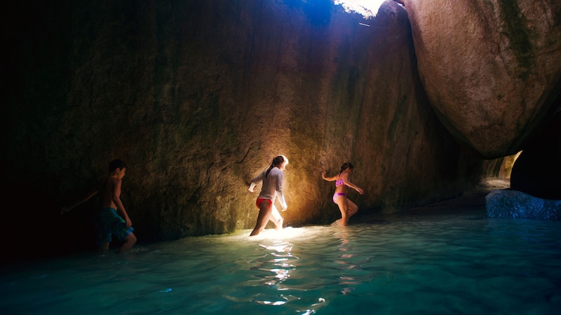 3 young people trekking through the waters of a cave in Tortola, British Virgin Islands