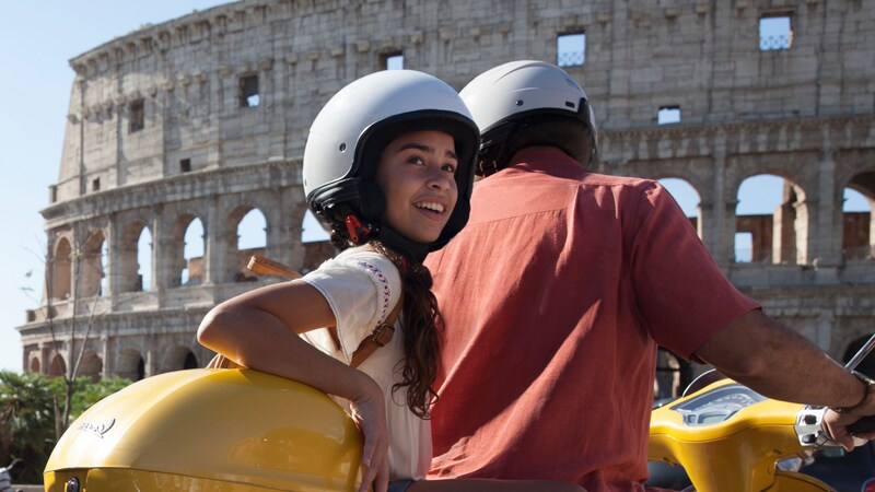 A man and a child riding on a motor scooter next to the Colosseum in Rome