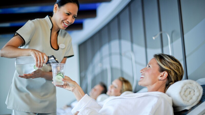 A woman relaxing in a spa while an attendant pours water into her glass
