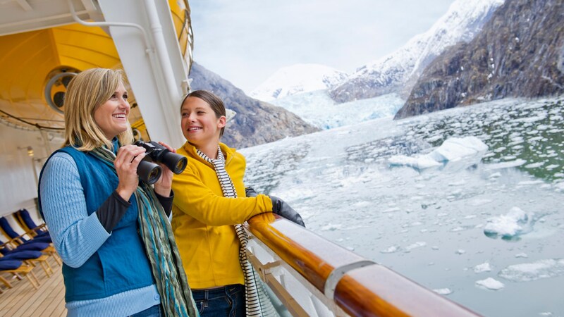 A woman holding binoculars standing next to a child on the deck of a Disney cruise ship