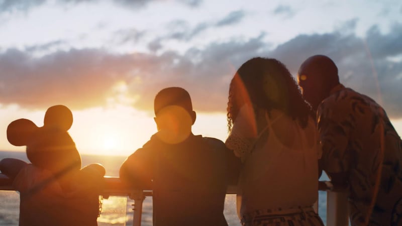 A family of 4 standing on the deck of a Disney cruise ship at sunset