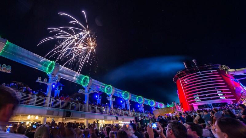 A crowd watching a nighttime fireworks show on the deck of a Disney cruise ship