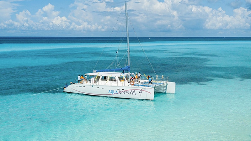 A catamaran with the words ‘Aqua Dream 4’ anchored in clear, shallow water